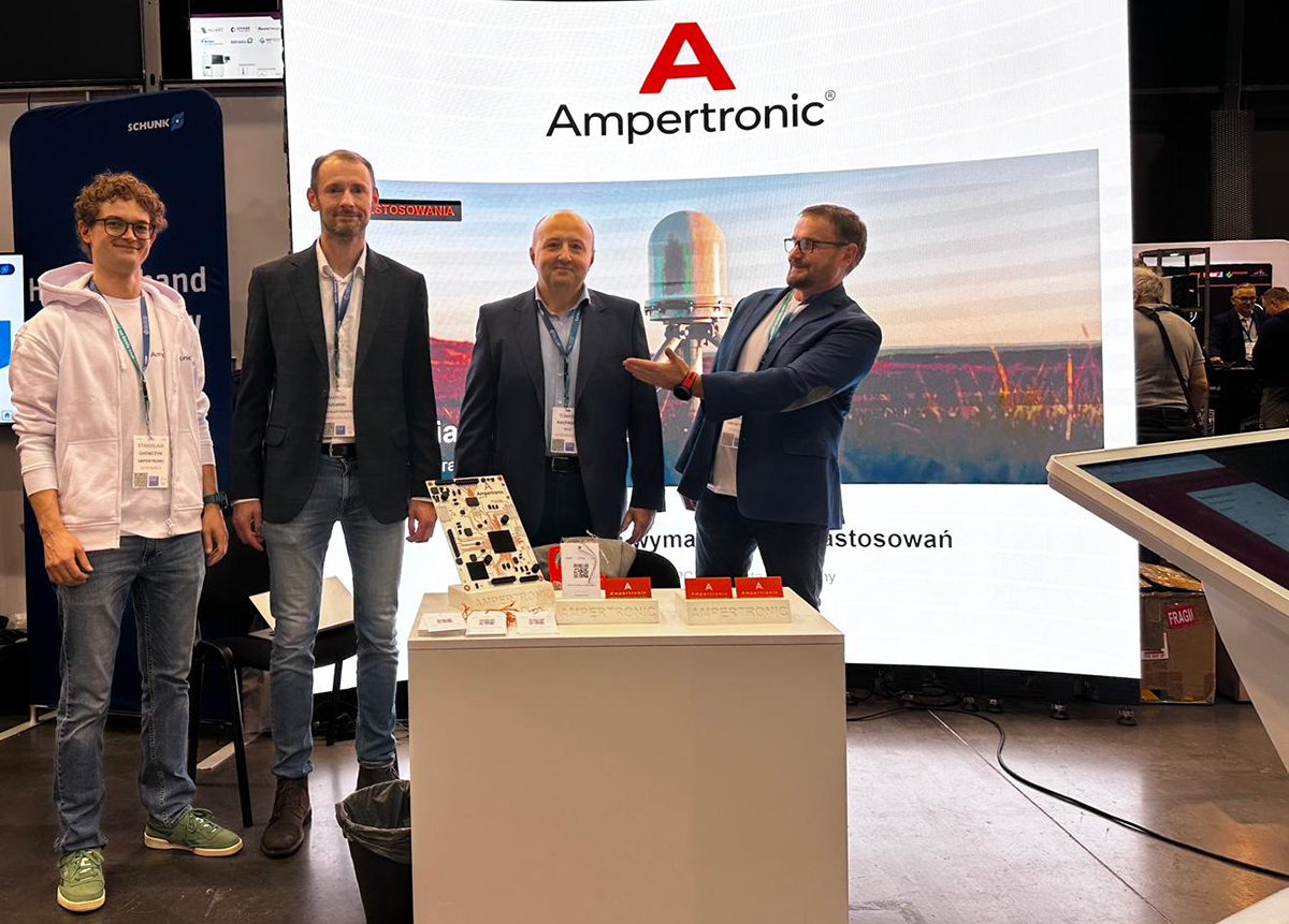 Goście i zespół Ampertronic przy stoisku na TEK.day Gdańsk 2026. Oryginalne zdjęcie wykorzystane w relacji z targów; widoczne ściana LED, model PCB i ekran dotykowy.